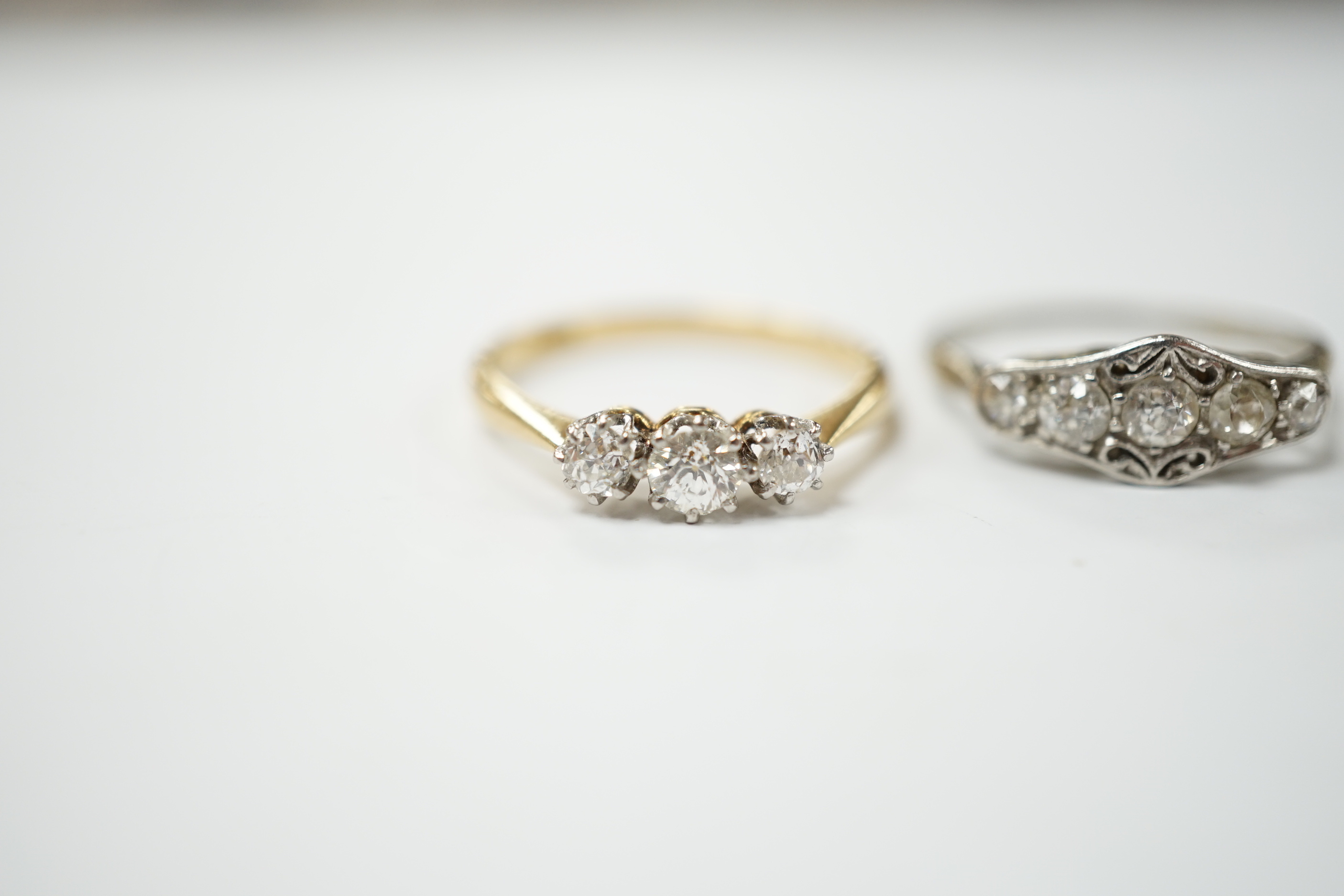 An 18ct gold three stone diamond ring, size M and a white metal five stone diamond dress ring, size M